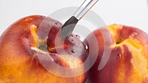 The artist paints with a brush on peaches. The artist`s brush close-up. Fresh juicy peaches on a white plate