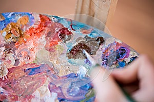 Artist paints a picture of oil paint brush in hand with palette closeup