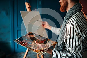 Artist with palette and brush in front of easel
