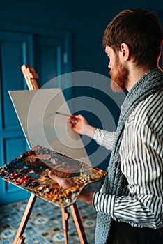 Artist with palette and brush in front of easel