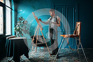 Artist with palette and brush paint on easel