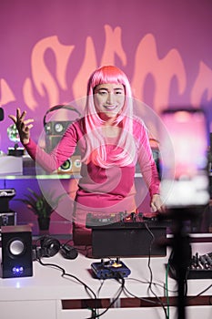 Artist with pink hair having fun in studio while performing techno song using professional mixer console