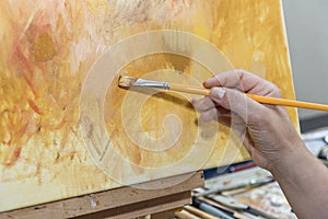 Artist`s hand holding yellow brush and canvas