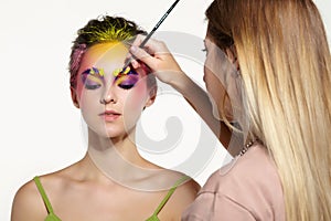 Artist`s hand with paintbrush painting beautiful girl`s brows make-up
