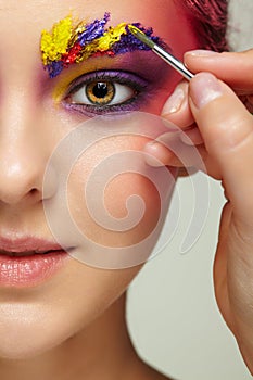 Artist's hand with paintbrush painting beautiful girl's brows make-up