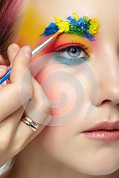 Artist`s hand with paintbrush painting beautiful teen girl`s brows make-up