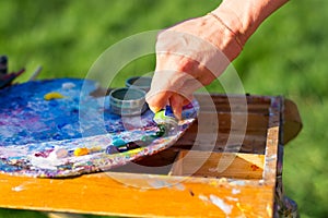 The artist`s hand, which squeezes the oil paint from the tube into the palette on the easel