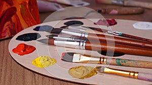 Artist`s palette with many colorful paints and brushes on wooden table, closeup