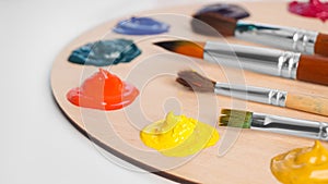 Artist`s palette with samples of colorful paints and brushes on white table, closeup