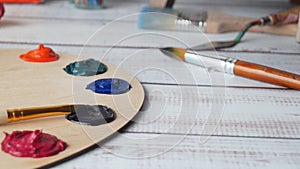 Artist`s palette with samples of colorful paints and brushes on white wooden table, closeup