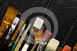 Artist`s tools, brushes in paint are in a row on a black wooden background.