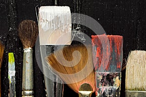 Artist`s tools, brushes in paint are in a row on a black wooden background.