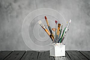 Artist`s tools, brushes, paints and a palette lie on a black wooden table on a gray fabric background.
