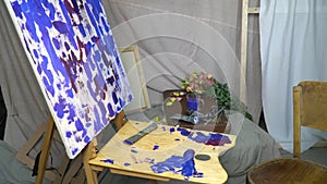 The artist`s workplace, canvas standing on a wooden easel, around scattered brushes, tubes of paint and flowers