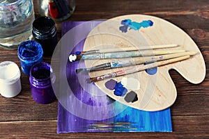 Artist`s workshop. Top view of paintbrushes palette and acrylic paints with white canvas. Set of brushes and oil paints. Art pictu