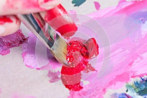 The artist squeezed the paint onto the palette and mixes the pink paint with a synthetic brush