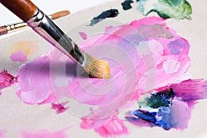 The artist squeezed the paint onto the palette and mixes the pink paint with a synthetic brush
