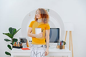 Artist standing in front of her work desk with notepad and crayons in hands