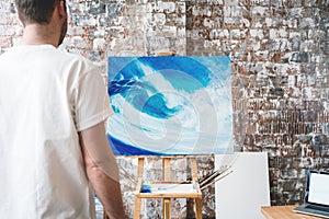 Artist stands in front of the easel with a canvas and considers his work
