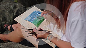 artist woman is drawing seascape with sailboats, using aquarell dyes