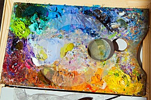 Artist wooden palette, mess of fresh bright colorful oil paints mixed in disorder, summer painting plein air