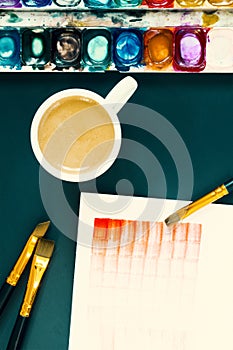 Artist work place. Coffee break on the lesson of watercolor painting. Paper, palette, acrylic paintbrush and a cup of coffee. The