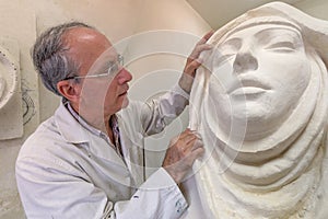 Artist at work in studio on a sculpture of face