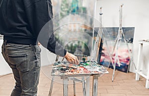 Artist is working on a painting in the studio. The back of the artist\`s husband, mixes the oil paint on a palette against the