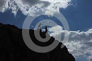 Artistic angel figure and figurine silhouette on top of high mountain rock. Help or fight statue.