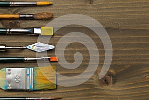 Artistic art supply utensils with brushes on brown wooden background with copy space flat lay top view from above