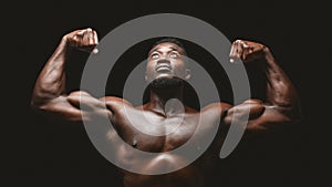 Artistic black athlete flexing biceps over black background