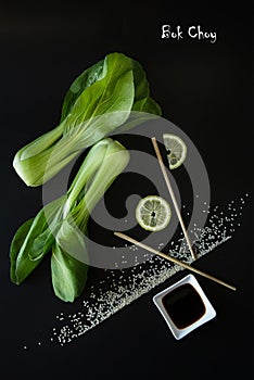 Artistic composition of Asian Food Products - Bok Choy , soy sauce, lemon end sesame seeds on a black background