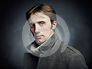 Artistic dark portrait of the young beautiful man in a gray coat