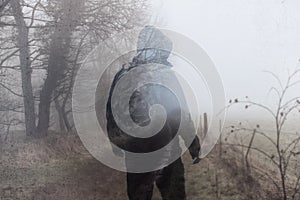 An artistic, double exposure of a hooded man on a country path on a moody foggy winters day. With a grunge, blurred edit