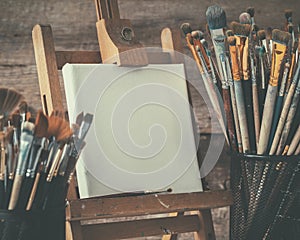 Artistic equipment: artist canvas on easel and paint brushes.