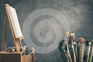 Artistic equipment in a artist studio: artist canvas on a wooden easel, paint tubes and paint brushes