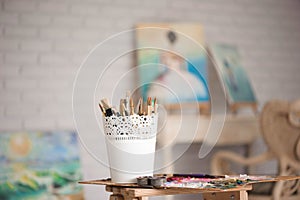 Artistic equipment: easel, paint brushes, tubes of paint, palette and paintings on work table in a artist studio