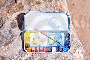 Artistic equipment: paint brushes, palette and paintings on rock in nature at sunny summer day - creation, drawing and freedom con