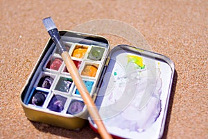 Artistic equipment: paint brushes, watercolors paintings on sand background at sunny summer day - creation, drawing and freedom co