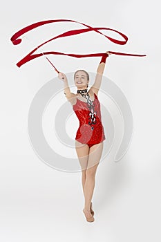 Artistic girl in red sportswear doing rhythmic gymnastics with ribbon, white background