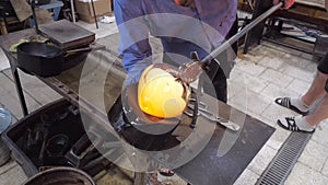 Artistic glassmaker shapes molten glass with wooden tool. The blower turning with a glasspipe in supporting fork