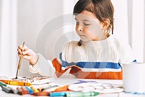 Artistic little girl painting and drawing with pencils and watercolor on white desk at home.