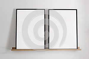 Artistic mockups template. Two black vertical picture frames on bamboo wooden shelf. White wall background. Posters at