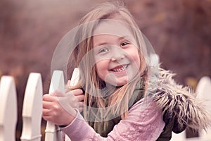 Artistic outdoor portrait of a cute blond girl holding on to a fence