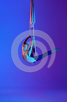 Artistic performance. Young man, acrobat training with aerial ribbons, doing gymnastics tricks against gradient blue