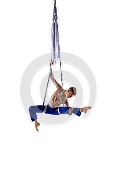 Artistic performance. Young man, acrobat training with aerial ribbons, doing gymnastics tricks against white studio