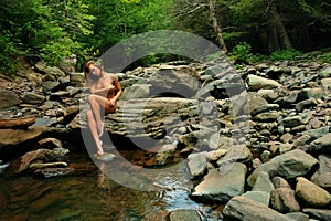 Artistic photo of nude elegant young woman posing at mountain river