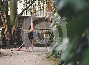 Artistic photo of an unrecognizable female yoga teacher in Revolved or Twist Wide Legged Forward Bend Pose in a terrace of a