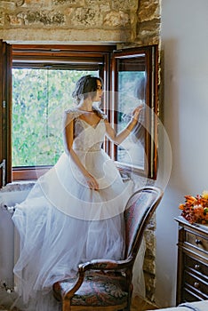 Artistic processing Fantasy girl princess in WHITE WEDDING dress stands in medieval CASTLE room looking vintage window