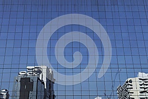 Artistic reflection of various buildings on blue reflective glass curtain wall building facade under clear bright daylight